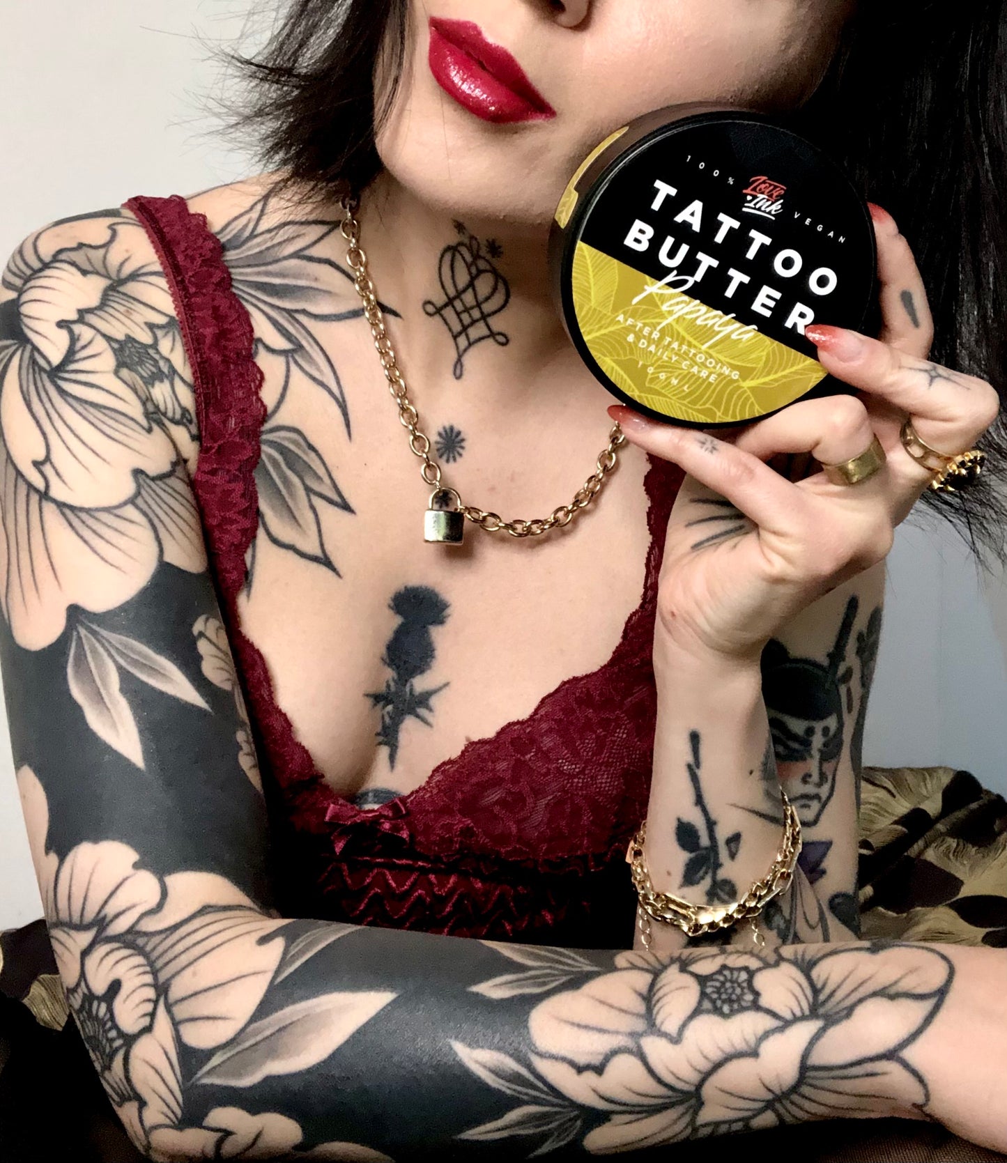 Person holding a jar of Tattoo Butter Papaya by LoveInk close to their face, showcasing detailed tattoos and emphasizing the product's connection to tattoo care.